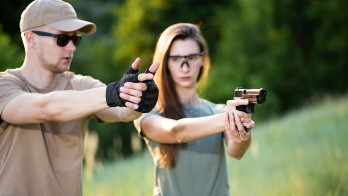 The instructor teaches the girl to shoot a pistol at the range