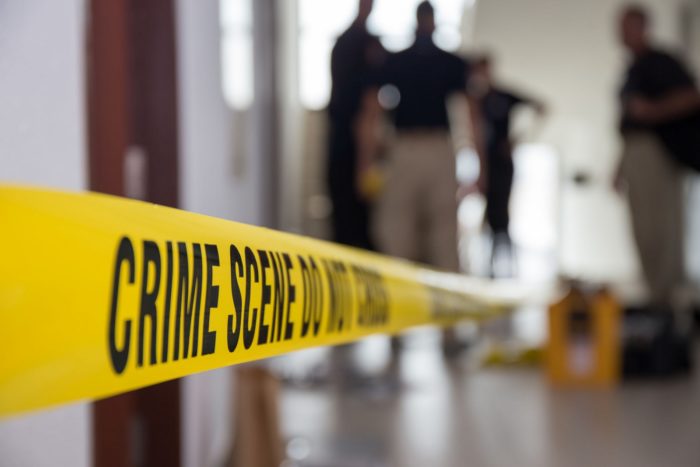 Crime scene tape in building with blurred forensic team backgrou