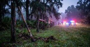Pickaxe leaning against a fence in a grassy field with flashing police vehicles in the foggy background